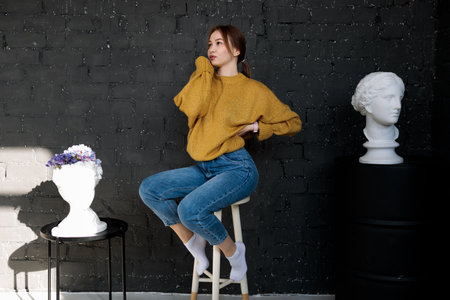a young woman in a full-length photo is sitting on a chair in casual clothes and posing for a photo...
