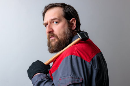 a middle-aged man turns around with a hammer on his shoulder and looks attentively. bearded...