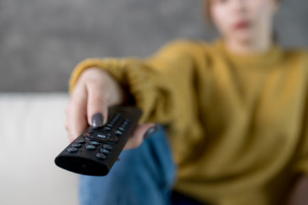 shallow depth of field remote control in a woman's hand, watching TV at home in a cozy place. this...