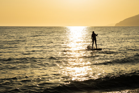 silhouette of a man on an inflatable board at sea, an oar in a man hand against the sunset backgroundの写真素材