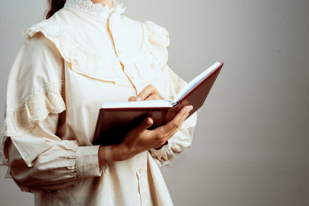 A woman is reading a book with her hand on the page. She is wearing a white blouse and a lace collarの写真素材