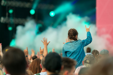 A girl is standing in a crowd of people, holding her hands up in the air. The crowd is cheering and the atmosphere is livelyの写真素材