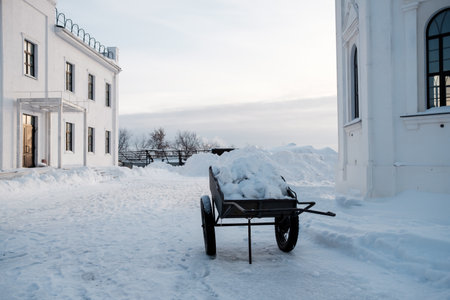 A snow covered cart is sitting in front of a white building. The cart is full of snow and he is abandoned. The scene is quiet and peaceful, with the snow covering the groundの写真素材