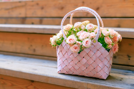 A pink basket filled with flowers sits on a wooden staircase. The basket is decorated with a pink handle and is filled with a variety of pink flowers. Concept of warmth and beautyの写真素材