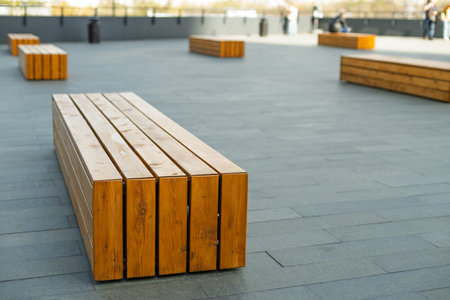 A row of wooden benches sit on a gray concrete surface. The benches are empty and the scene is quietの写真素材