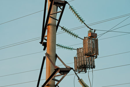 A tall pole with a large metal box on top of it. The box is connected to a power line. The pole is...