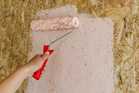 A person is painting a wall with a roller. The wall is made of wood and the paint is pinkの写真素材