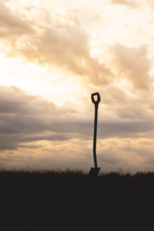 A shovel stuck in the ground against the sunset.の写真素材