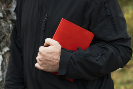 A man holds a red book in his hand. The man is wearing a black jacketの写真素材