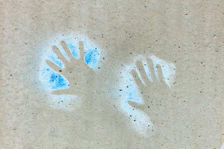 Two hands on a concrete surface, with one hand being blue and the other hand being white. The blue...