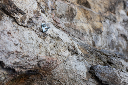 A small silver object is sitting on a rock. The rock is gray and has a rough texture. The object is...