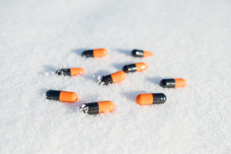 A pile of pills are scattered on the snow. The pills are orange and black. Concept of disorder and chaosの写真素材