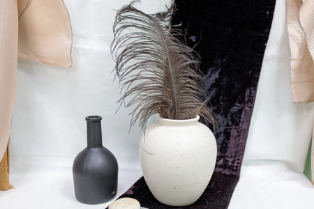 A black vase and a white vase are on a table. The black vase is empty and the white vase has a feather in itの写真素材