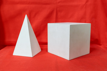 Two white shapes, one of which is a pyramid, are placed on a red background. The pyramid is larger...