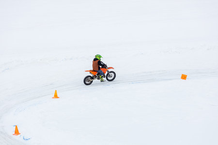A young man is riding a dirt bike on a snowy road. The snow is piled up on the ground, and the man...