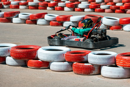 A man is driving a go kart on a track with red and white tires. The tires are piled up in the backgroundの写真素材