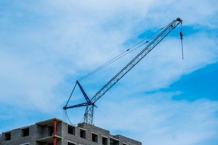 A crane is lifting a large object in the sky. The sky is blue and there are some cloudsの写真素材