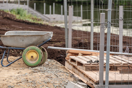 A wheelbarrow is sitting on a pile of dirt next to a wooden pallet. The scene suggests that someone...