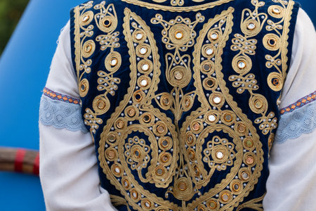 A person is wearing a blue vest with gold embroidery. The vest is decorated with many small, round,...