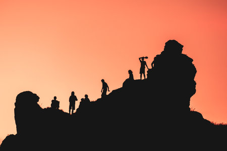 A group of people are standing on a mountain, silhouetted against a beautiful sunset. Scene is...