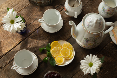 Tea party. Porcelain tea set and sliced fresh lemons on plate standing on wooden table.の写真素材