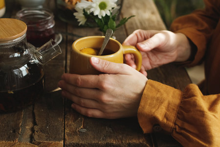 Rustic morning breakfast. Person drinking tea with lemon slice. Female hands holding mug of tea.の写真素材