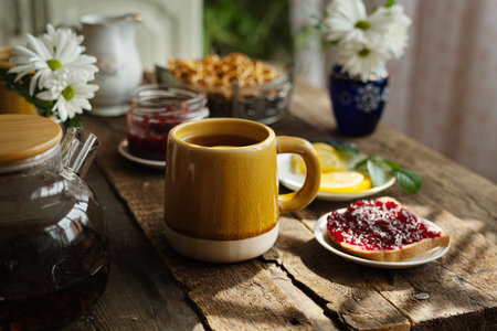 Table set for morning breakfast on kitchen. Ceramic mug of tea with lemon and toast with jam on...