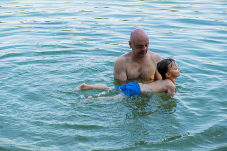 Summer outdoor activities. Father teaches his little son to swim in lake.