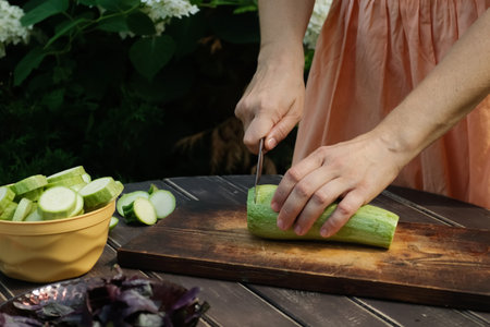 Woman is slicing zucchini on a cutting board in backyard.の写真素材