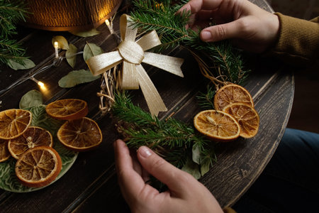 Hands making Christmas wreath with bow, dried oranges and spruce twigs.の写真素材