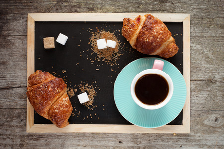 Breakfast with coffee and fresh croissants on old slate chalk board, top view, wooden backgroundの写真素材