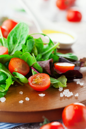 Fresh salad with cherry tomatoes and spinach, arugula, romaine and lettuce on a wooden chopping board on rustic white background, selective focusの写真素材
