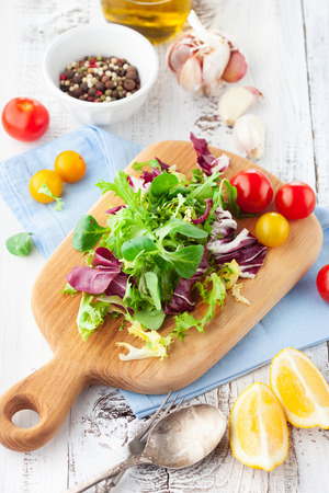 Fresh salad with cherry tomatoes, spinach, arugula, romaine and lettuce on a wooden chopping board on rustic white background, selective focusの写真素材