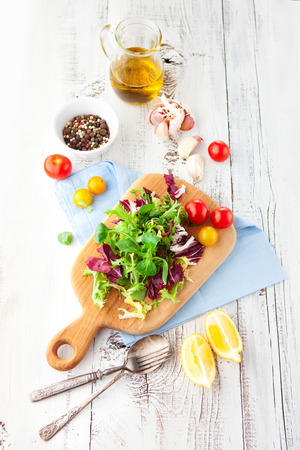 Fresh salad with cherry tomatoes, spinach, arugula, romaine and lettuce on a wooden chopping board on rustic white background, selective focusの写真素材