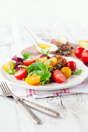 Fresh salad with cherry tomatoes, spinach, arugula, romaine and lettuce in a plate on white wooden backgroundの写真素材