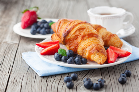 Delicious breakfast with fresh croissants and ripe berries on old wooden background, selective focusの写真素材
