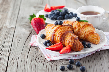 Delicious breakfast with fresh croissants and ripe berries on old wooden background, selective focusの写真素材