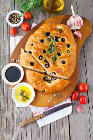 Freshly baked traditional Italian focaccia bread with rosemary and black olives on old wooden background, top viewの写真素材