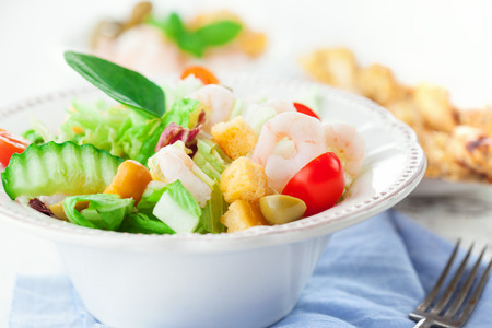 Healthy shrimp salad with mixed greens, olives and tomatoes on white wooden background, selective focusの写真素材