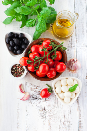 Ripe cherry tomatoes, fresh basil leaves, mozzarella cheese and olive oil for caprese salad on white wooden background, top viewの写真素材