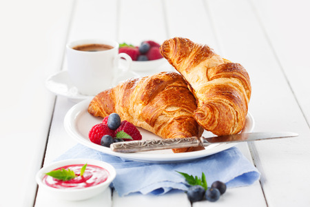Breakfast with cup of coffee, fresh croissants and ripe berries on white wooden background, selective focusの写真素材
