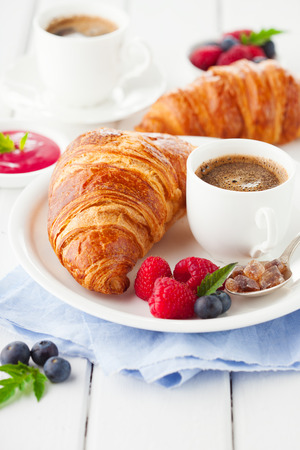 Breakfast with cup of coffee, fresh croissants and ripe berries on white wooden background, selective focusの写真素材