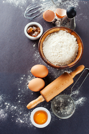 Ingredients and tools for baking - flour, eggs and rolling pin on the black background, top viewの写真素材