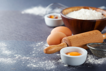 Ingredients and tools for baking - flour, eggs and rolling pin on the black background, selective focusの写真素材