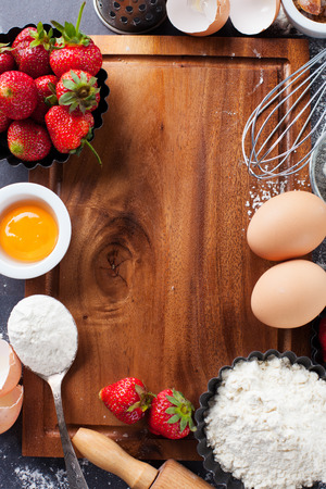 Ingredients and tools for baking - flour, eggs, rolling pin and fresh berries on the black background, top viewの写真素材