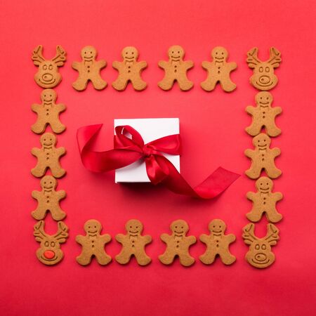 Christmas or new year composition. Gift inside frame made of winter gingerbread cookies on red...