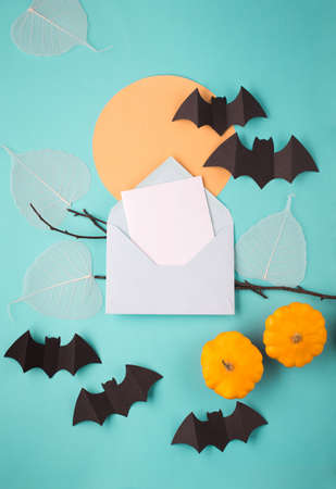 Halloween paper decorations on blue background. Black bats, tree branch and moon. Halloween concept. Flat lay, top view, overhead. Halloween party greeting card mockup with copy space. Empty blank card in paper envelope.の写真素材