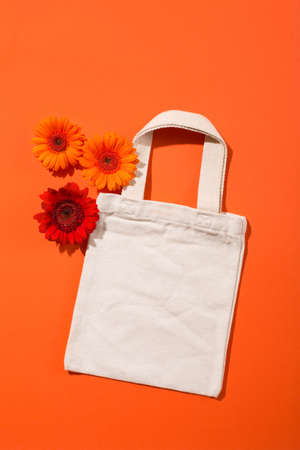 Mock up design bag concept. Top view of blank white tote bag canvas fabric with beautiful orange flower gerbera daisy. Cloth shopping sack mockup with copy space. Orange background.の写真素材