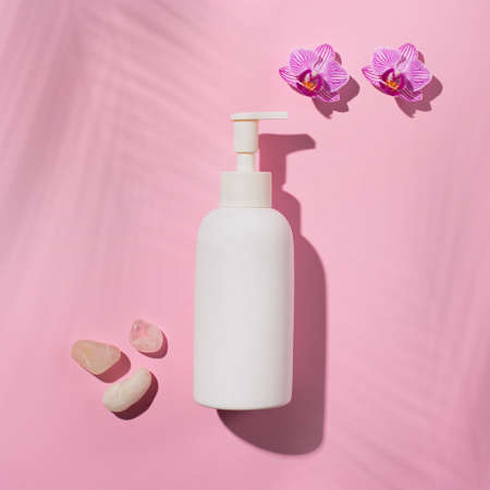 Minimal background for branding and product presentation. White cosmetic bottle with pink flower phalaenopsis orchid and shadow palm leaves. Beauty SPA branding mock-up.の写真素材