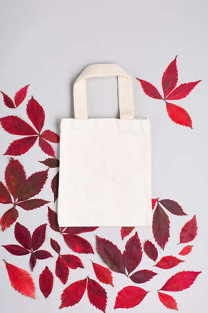 Mock up design bag concept. Top view of blank white tote bag canvas fabric with Red leaves wild grape. Cloth shopping sack mockup with copy space. Gray background.の写真素材